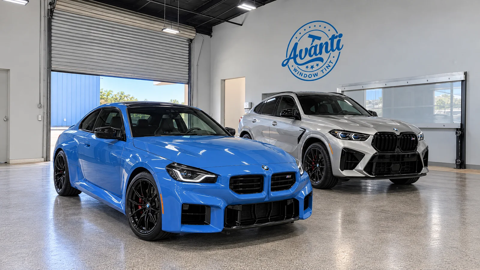 Zandvoort Blue BMW M2 and silver BMW X6 M with tinted windows inside the Avanti Window Tint shop in San Diego